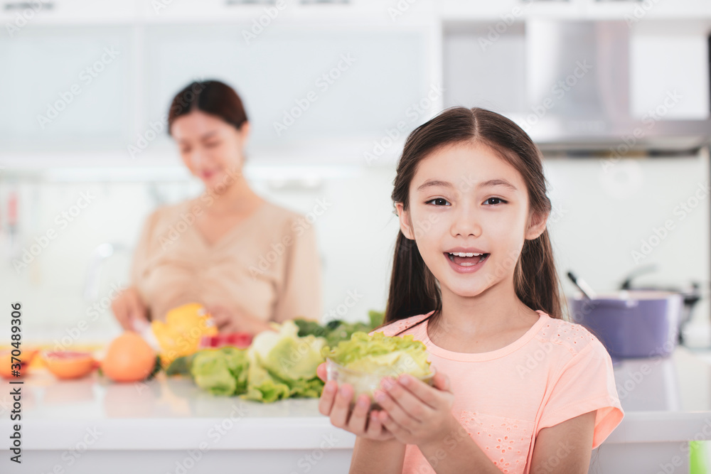 mother working at kitchen and daughter showing health food mother working at kitchen and daughter showing health food