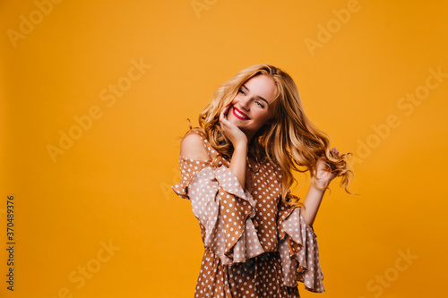 Dreamy smiling woman playing with her hair. Studio photo of amazing caucasian lady with red lips laughing on yellow background.