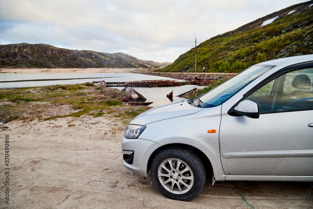 Small car standing on the side of road near wate of lake, river, fiord, sea and ocean.