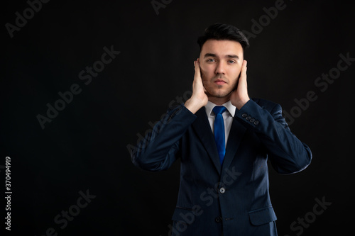 Portrait of business man wearing blue business suit and tie covering ears like deaf gesture
