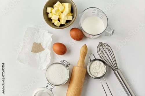 cooking food and culinary concept - rolling pin, butter, eggs, flour and cane sugar on table