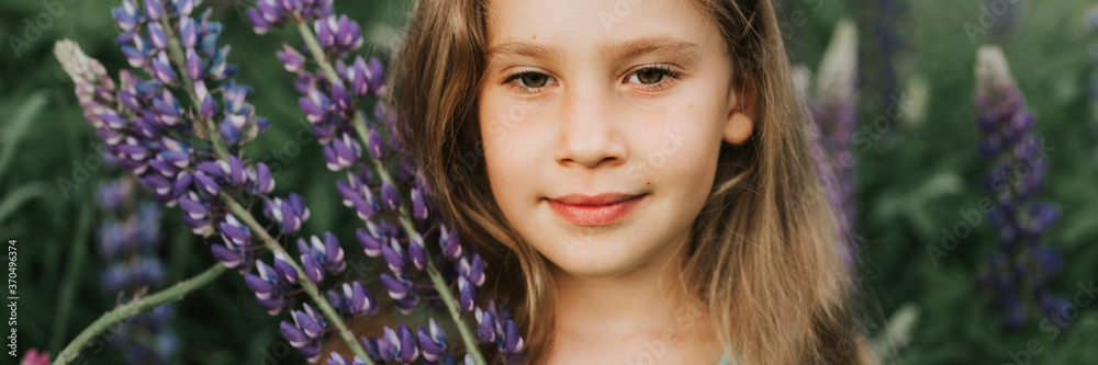 portrait of a cute little happy seven year old kid girl with bloom flowers lupines in a field in nature outdoor. banner portrait of a cute little happy seven year old kid girl with bloom flowers lupines in a field in nature outdoor. banner