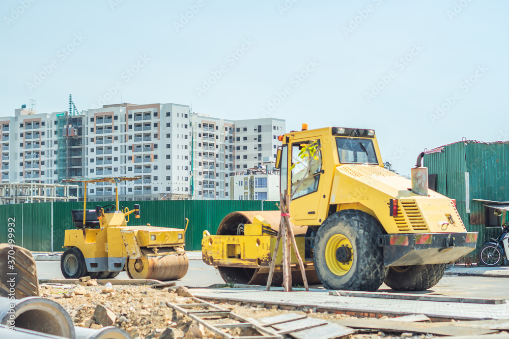 Large view on the big and small yellow road rollers working on the new modern multi-storey buildings district road construction site under blue sky. Civil building industry