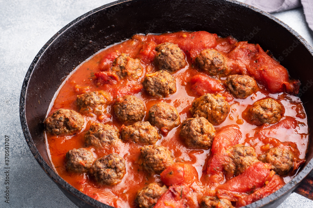 Delicious juicy Meatballs in tomato sauce are cooked in a cast iron pan. Close up Concrete background.
