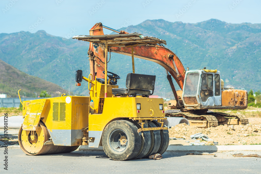 Large view on big yellow road rollers and other construction machinery in sunny day work on new modern district road construction site under blue sky and mountain background. Civil building industry Large view on big yellow road rollers and other construction machinery in sunny day work on new modern district road construction site under blue sky and mountain background. Civil building industry