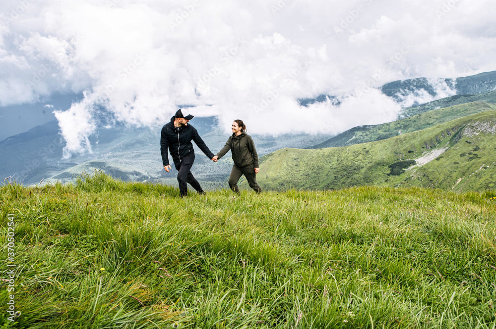 A couple in love walk holding hands on the top of mountain with a scenic view on the background