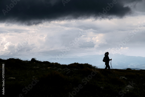Amazing silhouette photo of woman with a nordic walking sticks, a big grey cloud above her. Hiking, backpacking