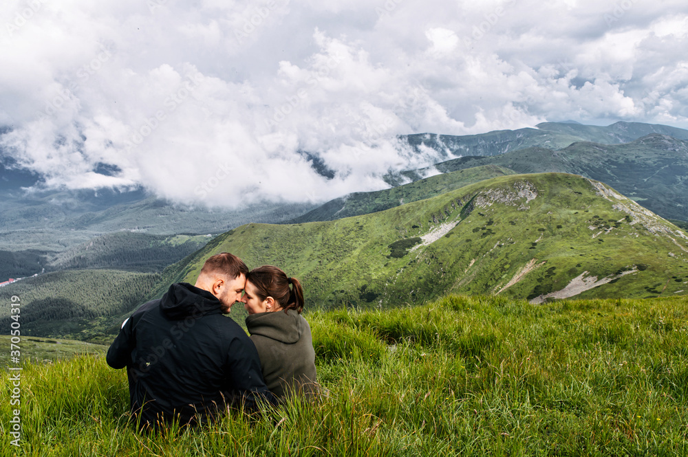 Couple in love is hiking in mountains. A man and a woman sit on the top of a mountain and hugging with a scenic nature view