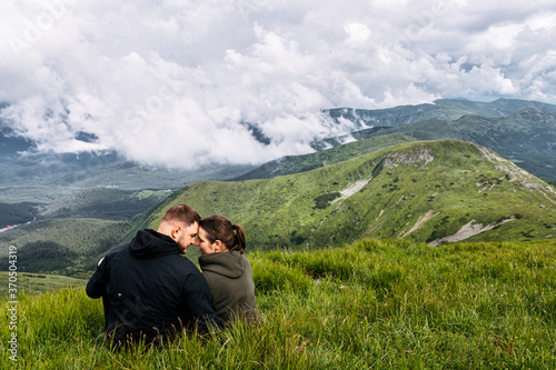 Couple in love is hiking in mountains. A man and a woman sit on the top of a mountain and hugging with a scenic nature view