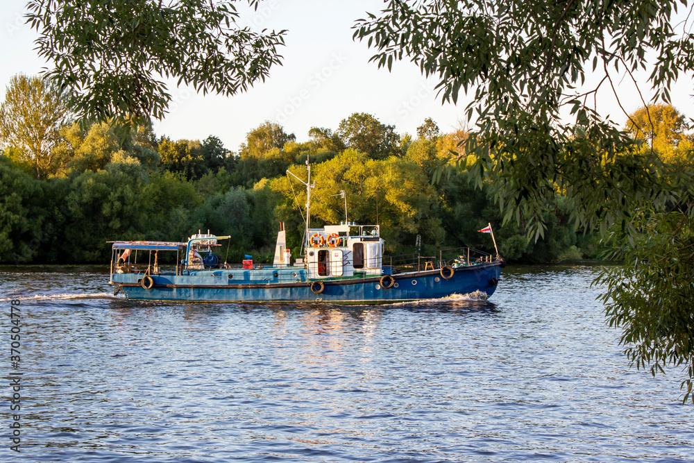 River tugboat is floating on the river. Trees grow on the banks of the river. Fork of the river. Landscape, summer day. Water excursions and trips. freight transport, copy space