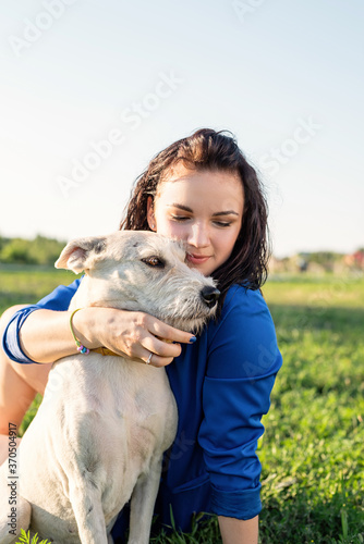 Beautiful young woman sitting in grass hugging her dog in the park