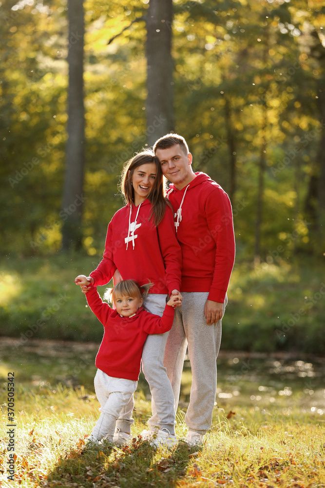 Fototapeta premium Portrait of happy family. Mom, dad and little daughter in autumn park. Young couple spending time together on vacation, outdoors. The concept of family holiday. Mother's, father's, baby's day.