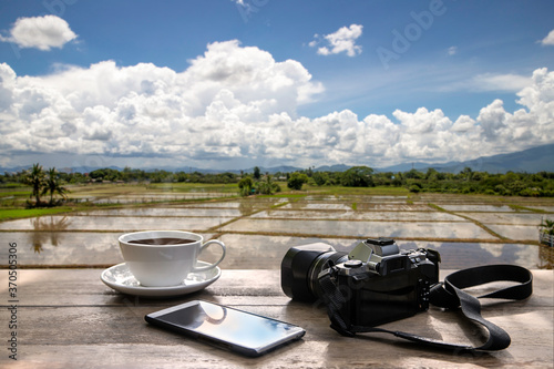cup of coffee with retro camera and mobile phone on wooden table with nature background 