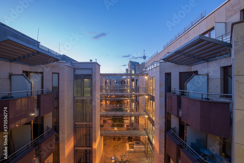 modern apartment building made of glass and steel and enriched with trees and flowers in the evening