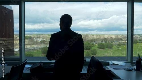 backlit silhouette of a Thoughtful businessman looking out the office window at a green landscape