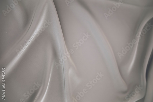 Close up picture of silk fabric with wavy holds in light grey color for fashion photography to show fabric shade. Textured background of soft satin for fashion clothes. Palette with grey shades.