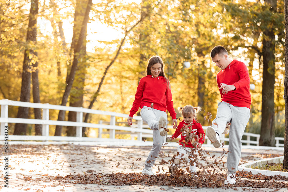 Fototapeta premium Mother, father and little daughter having fun in the autumn park. Young family spending time together on vacation, outdoors. The concept of family holiday.