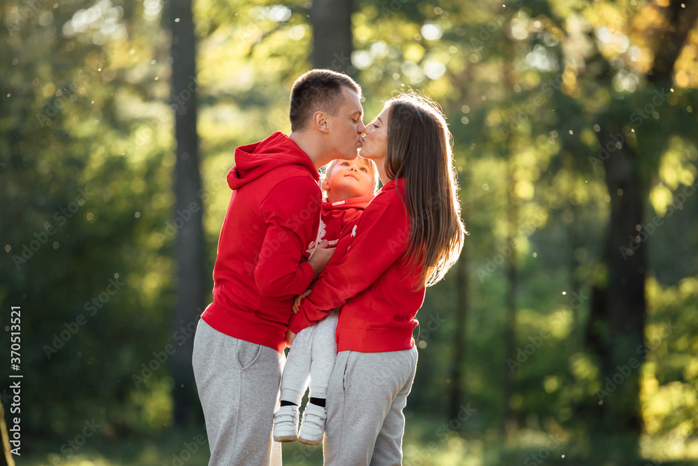 Mom, dad hugging daughter and kissing in the autumn park. Young family spending time together on vacation, outdoors. The concept of family holiday. Mother's, father's, baby's day. Mom, dad hugging daughter and kissing in the autumn park. Young family spending time together on vacation, outdoors. The concept of family holiday. Mother's, father's, baby's day.