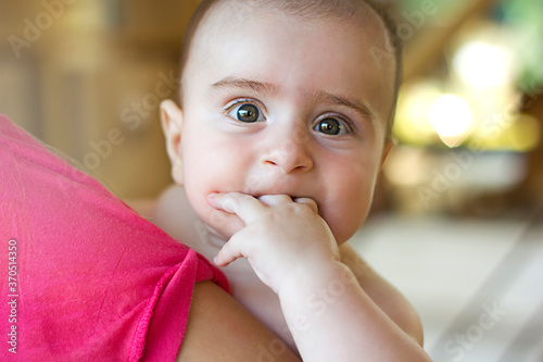 Cute little Baby boy putting the hand in mouth with his mom. Close up child portrait with mother. Looking at camera