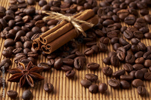 Roasted whole coffee beans, tied sticks of cinnamon and anise on a bamboo mat