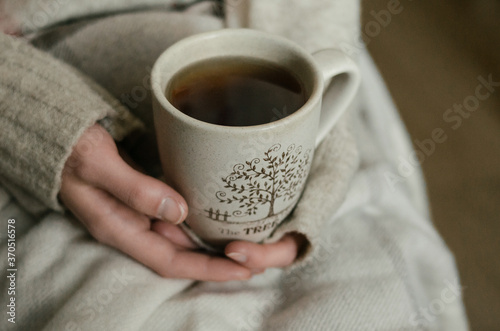 Tea in autumn. Girl holds mug of dark tea on beige plaid background. Cold morning in fall 