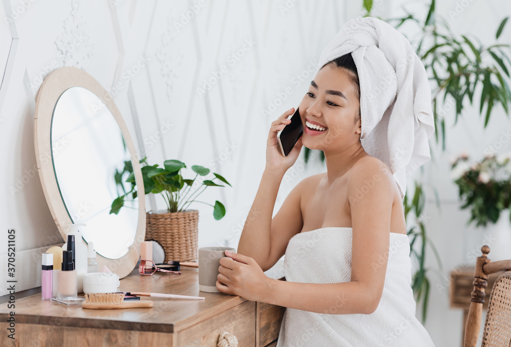 Happy asian girl talking on phone, sitting next to mirror Happy asian girl talking on phone, sitting next to mirror