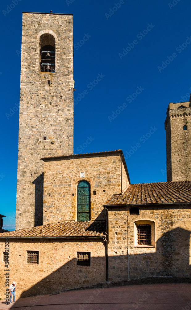 Picturesque scene of an old man with hat walking up a slope in the famous medieval hill town San Gimignano in Tuscany with the campanile della Collegiata in the background. 