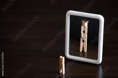 selfish concept. small clothespin seeing himself in the mirror as big king with crown