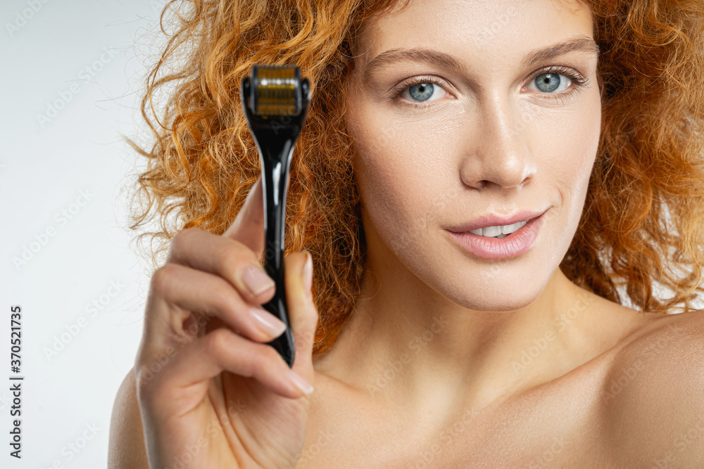 Beautiful young woman with red hair holding face massager Beautiful young woman with red hair holding face massager
