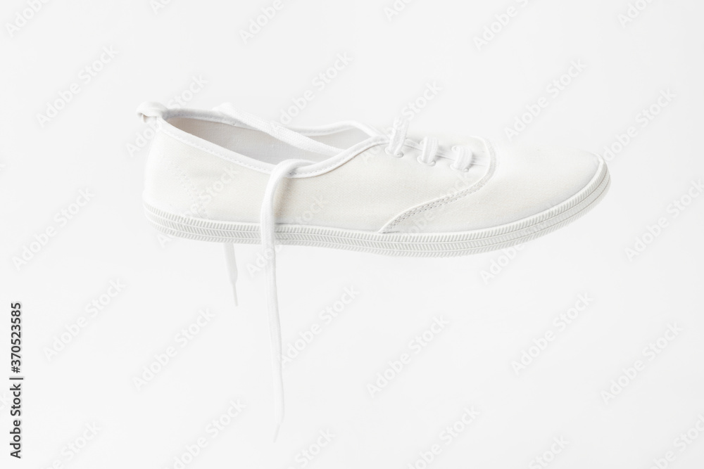 White canvas laced unisex plimsoll shoe on same color background with copy space. Classic casual sport footwear youth teenager urban fashion active lifestyle concept White canvas laced unisex plimsoll shoe on same color background with copy space. Classic casual sport footwear youth teenager urban fashion active lifestyle concept