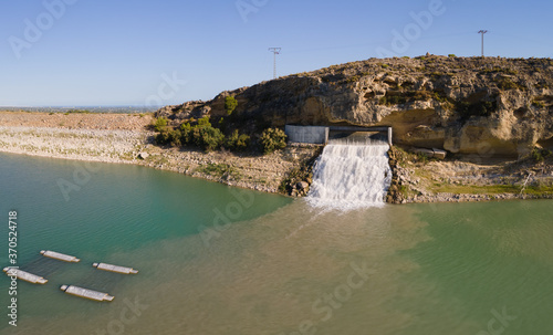 A waterfall on a reservoir above Crevillente. The water flows into the lake. In the background on the horizon the Mediterranean Sea with blue skies in summer.