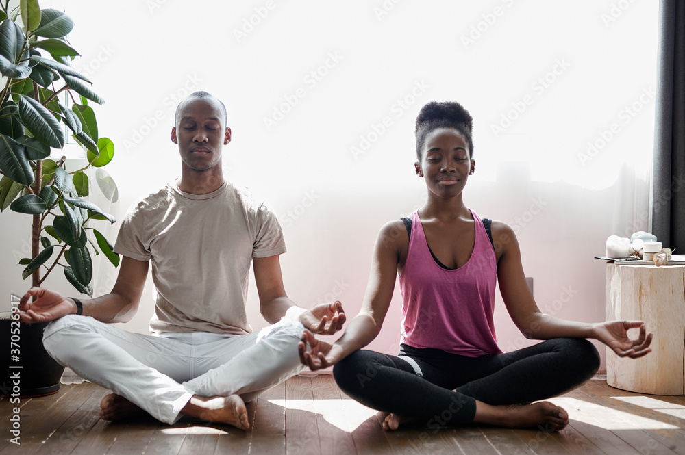 african ameican man and woman meditate, practice yoga together at home. keep calm and be happy. yoga, sport, healthy lifestyle concept