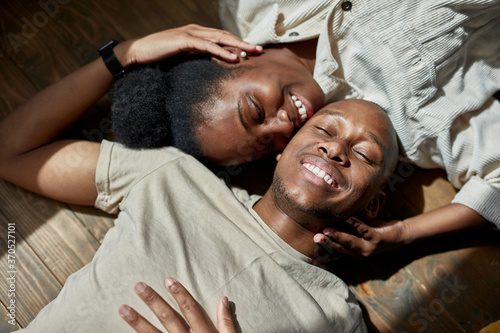 top view on attractive young african american married couple lying on the floor, they are posing at camera, man and woman in love, smile