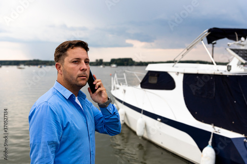 Man talking on the phone beside luxury yacht at port. Nautical and marine concept