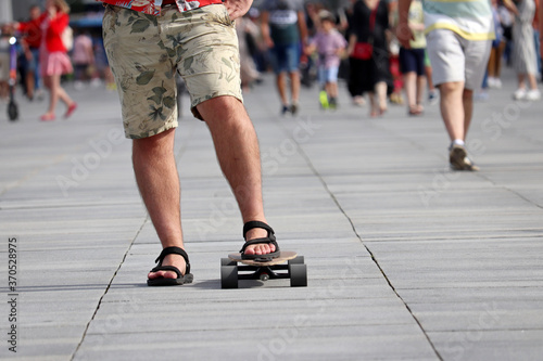 Skateboarding in a city, man in shorts with skateboard on a summer street on crowd of people background