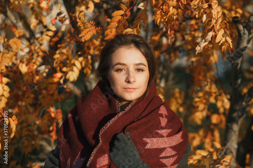 Outdoor fashion photo of young beautiful lady in red scarf and dark grey coat surrounded autumn landscape.