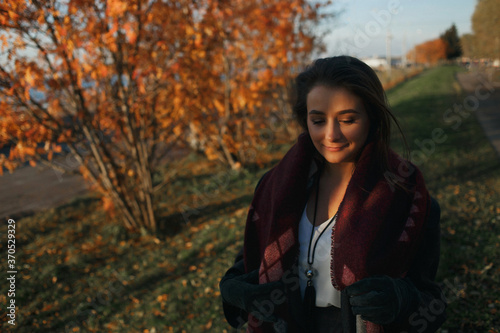 Outdoor fashion photo of young beautiful lady in red scarf and dark grey coat surrounded autumn landscape.