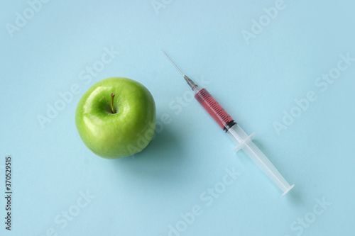 Green apple and syringe with GMO on a blue background.
