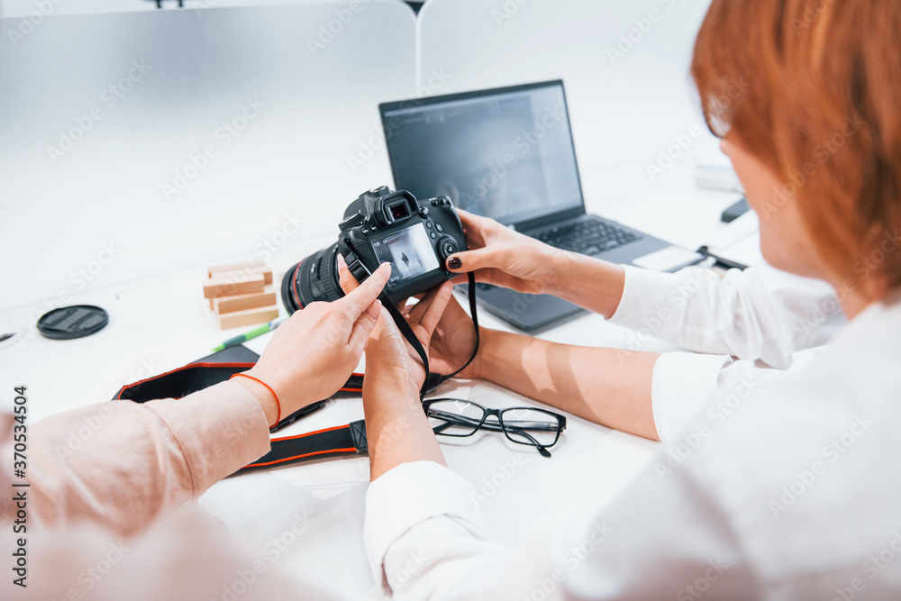 Two women sitting by the table and looking at photos that is in camera Two women sitting by the table and looking at photos that is in camera