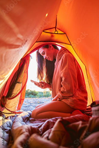 Beautiful young woman using cellphone in camp tent