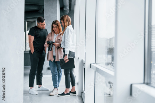 Group of people standing indoors together and looks at photos on camera