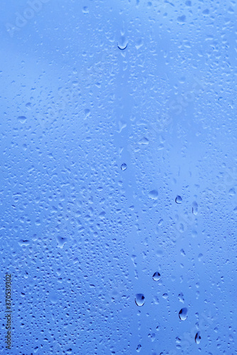 Autumn window with the texture of water drops against a cloudy blue sky. Glass background with drops of rain.