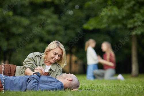 Portrait of loving adult couple laying on green grass in park and enjoying time together outdoors, copy space