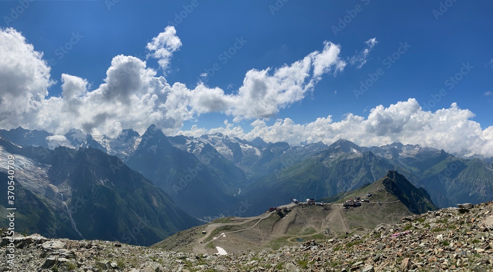 Obraz premium Snowy mountain against cloudy sky. From below white clouds floating on blue sky over mountain ridge covered with snow on sunny day in nature