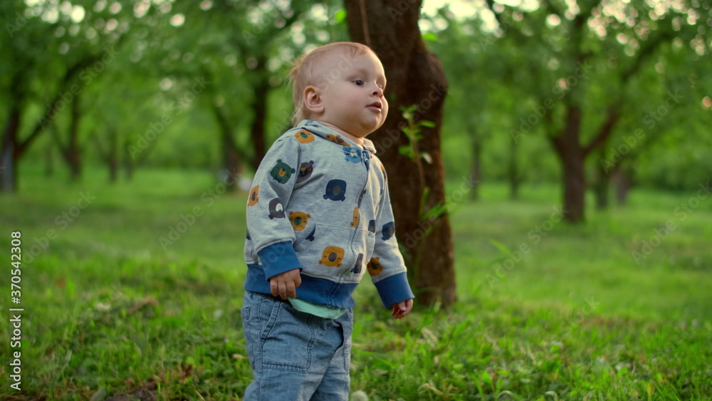 Cute kid boy falling on ground outdoors. Little baby standing in green park. Cute kid boy falling on ground outdoors. Little baby standing in green park.