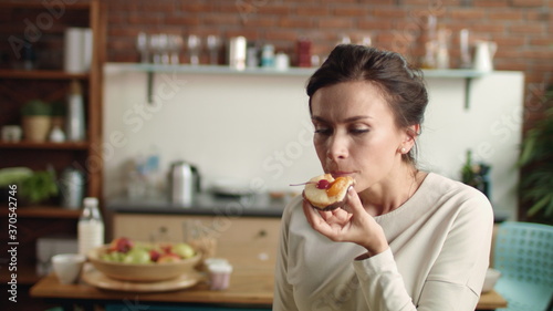 Woman looking at camera with fancy cake in hand. Girl biting dessert at home.