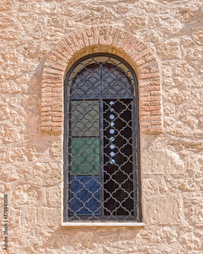 old arched window secured with iron grid on rough stone wall