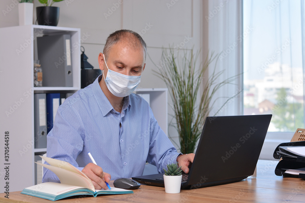 Businessman works in the office in a medical mask for coronavirus protection. New normal business practise of coronavirus covid-19 outbreak control Businessman works in the office in a medical mask for coronavirus protection. New normal business practise of coronavirus covid-19 outbreak control