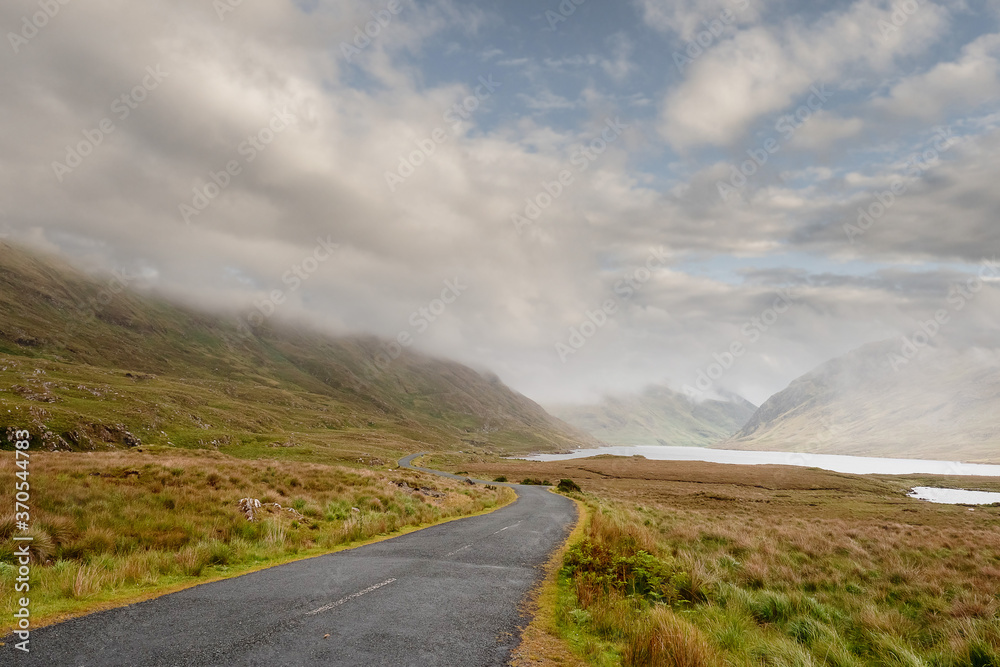 Small empty road leads into mountains. Low cloudy sky, Connemara, Ireland. Nobody. Travel concept Small empty road leads into mountains. Low cloudy sky, Connemara, Ireland. Nobody. Travel concept