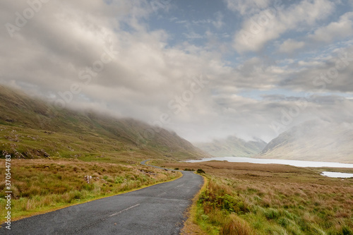 Small empty road leads into mountains. Low cloudy sky, Connemara, Ireland. Nobody. Travel concept
